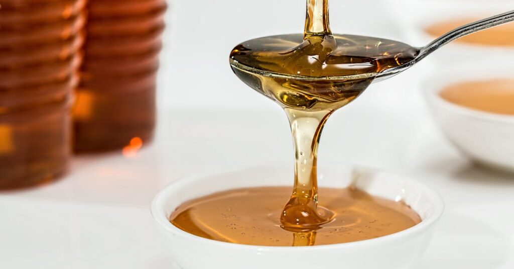 Delicious honey pouring slowly from a spoon into a white bowl, highlighting its golden hue and viscosity.
