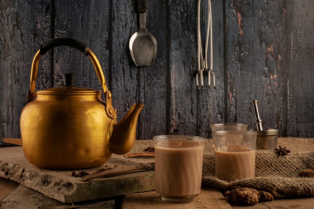 Charming setup featuring a brass kettle and glasses of Indian chai on a rustic table.