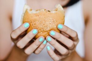 A close-up shot of hands with blue nails holding a sesame seed burger. Ideal for food blogs or fast food features.