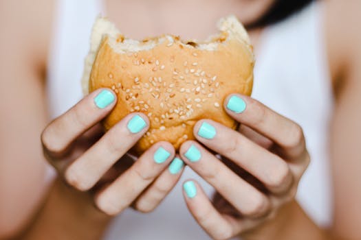 A close-up shot of hands with blue nails holding a sesame seed burger. Ideal for food blogs or fast food features.