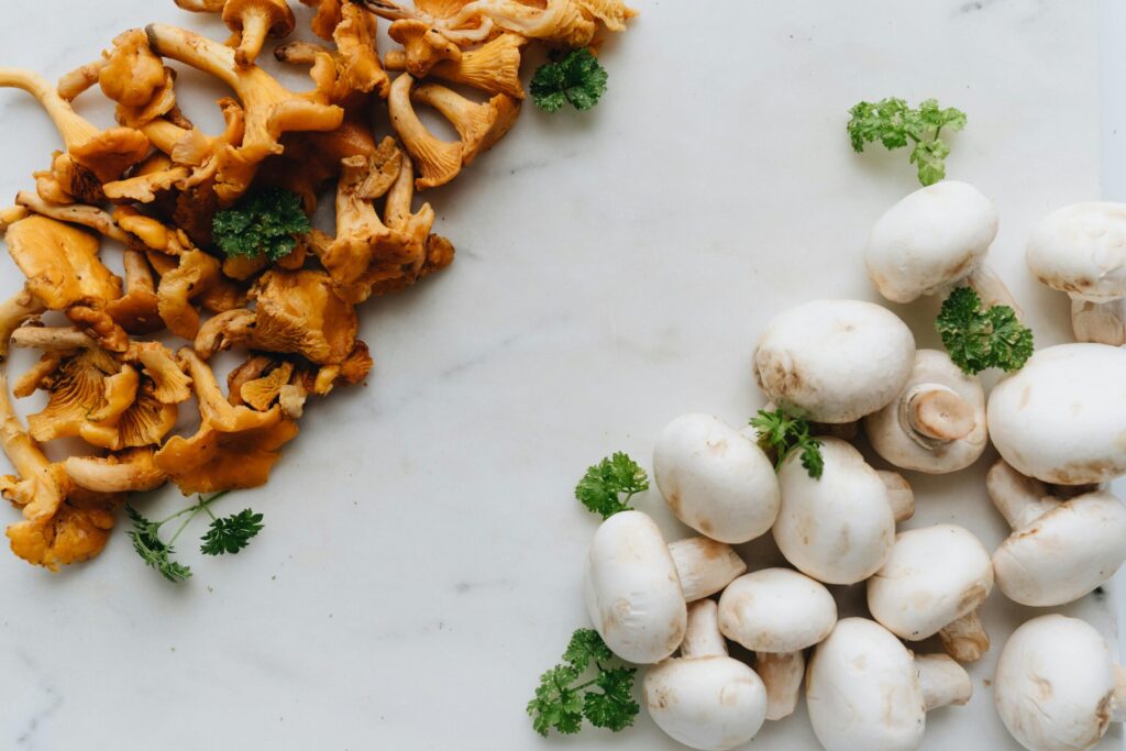 Fresh chanterelle and white mushrooms on marble with parsley, perfect for gourmet cooking.
