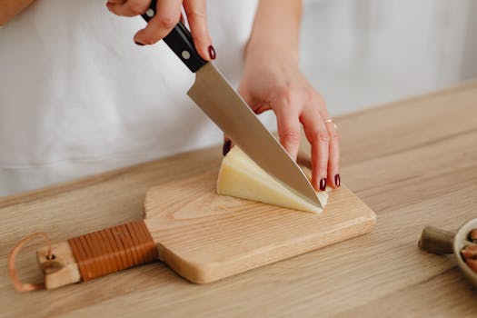 Close-up view of a person cutting cheese on a wooden board with a knife.