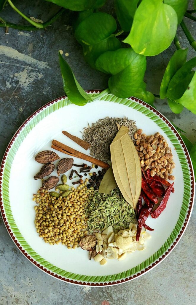 Colorful assortment of spices displayed on a plate with green leaf background.
