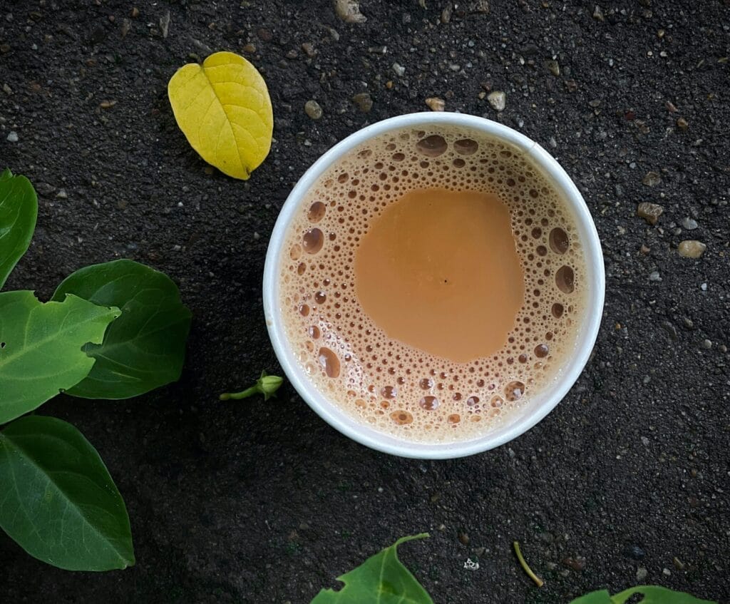 A close-up of a frothy coffee cup on a textured surface with green and yellow leaves nearby.