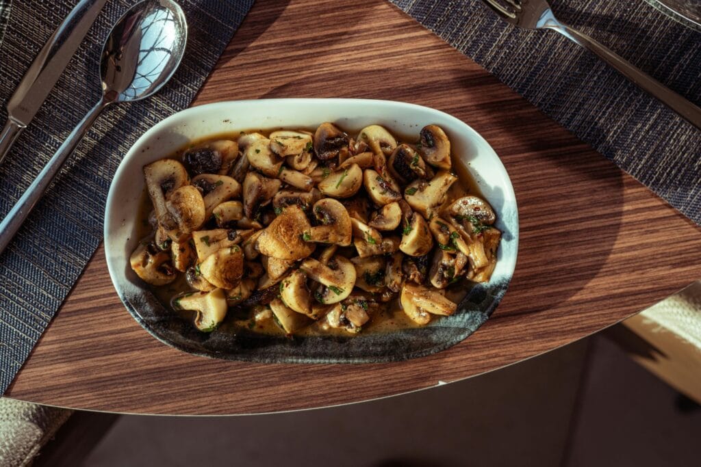 Top-down view of sautéed mushrooms in a white dish on a wooden table.