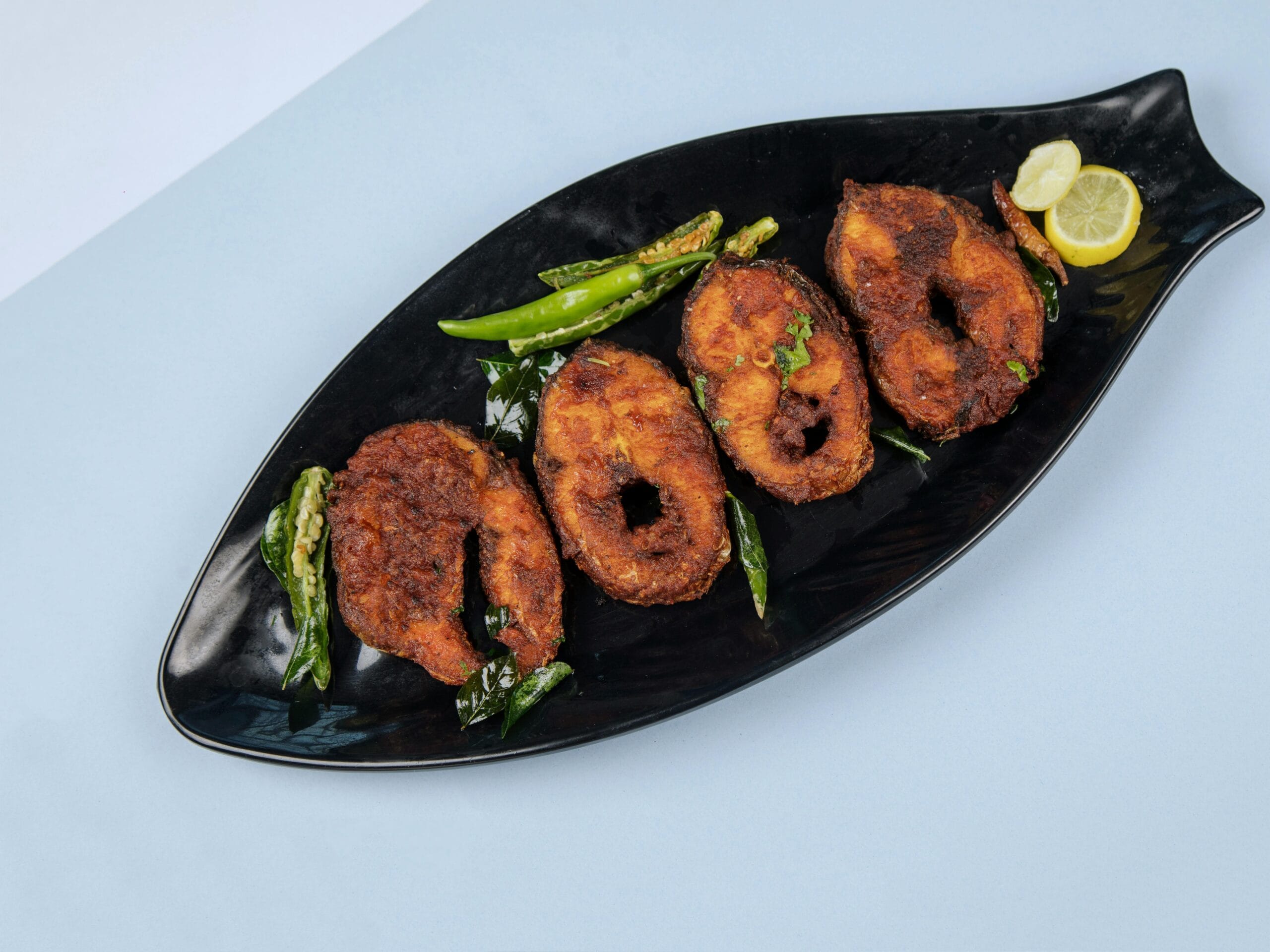 Delicious crispy fried fish served with lemon and chili on a stylish black plate.
