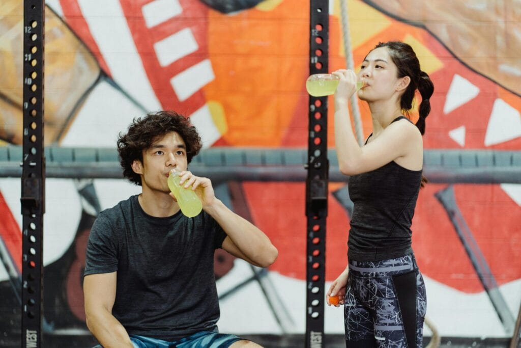 Asian couple in activewear drinking yellow beverages at an indoor gym.