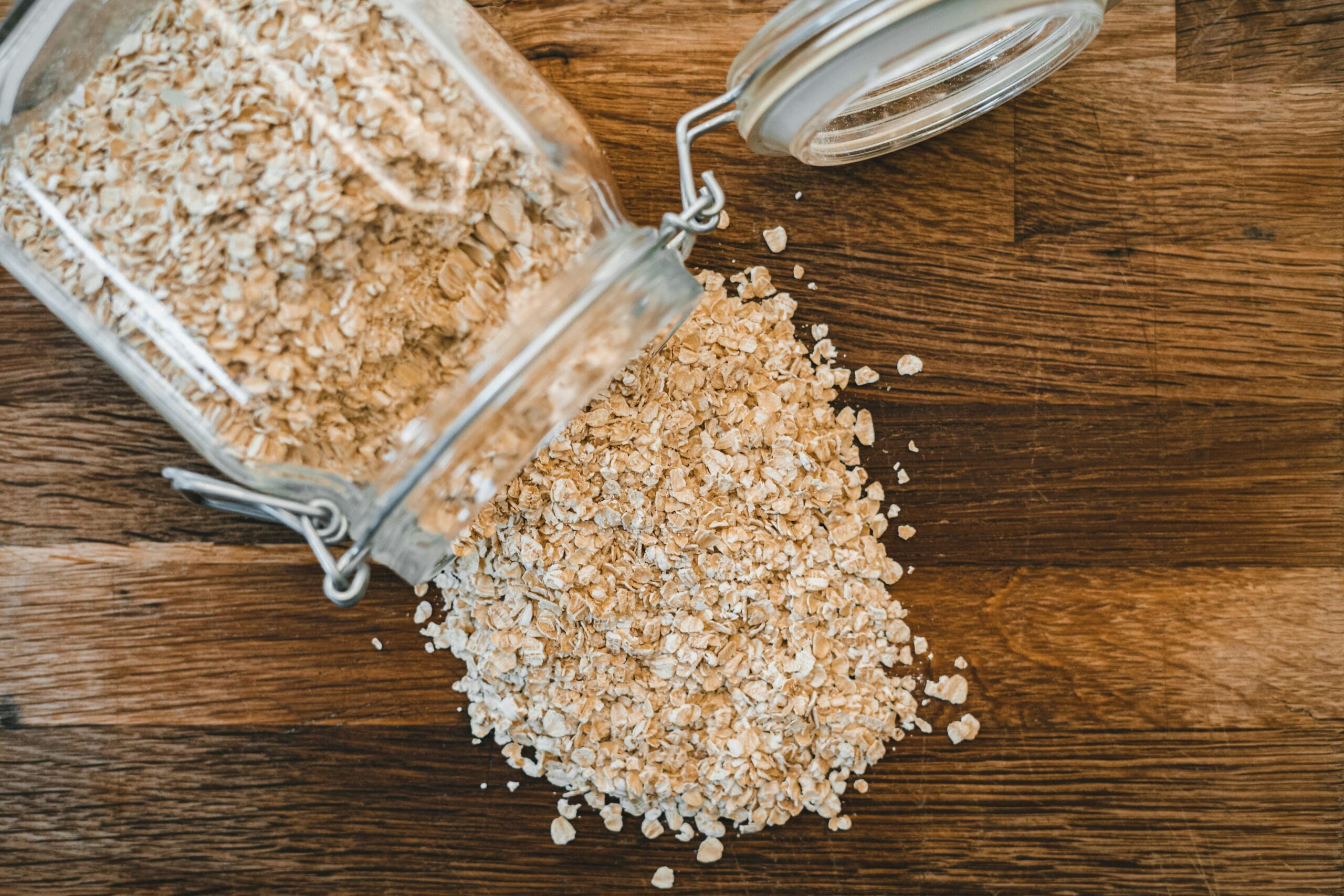 Close-up of rolled oats spilling from a jar on a wooden surface, showcasing healthy food.