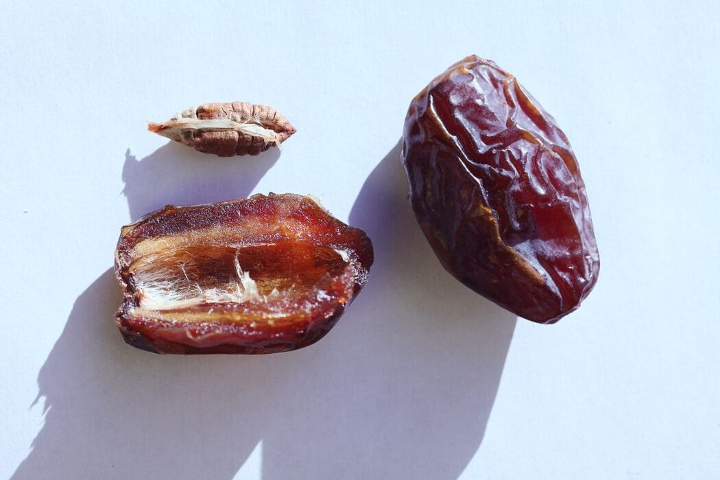 Close-up flat lay of whole and half dates with seed on a white background.