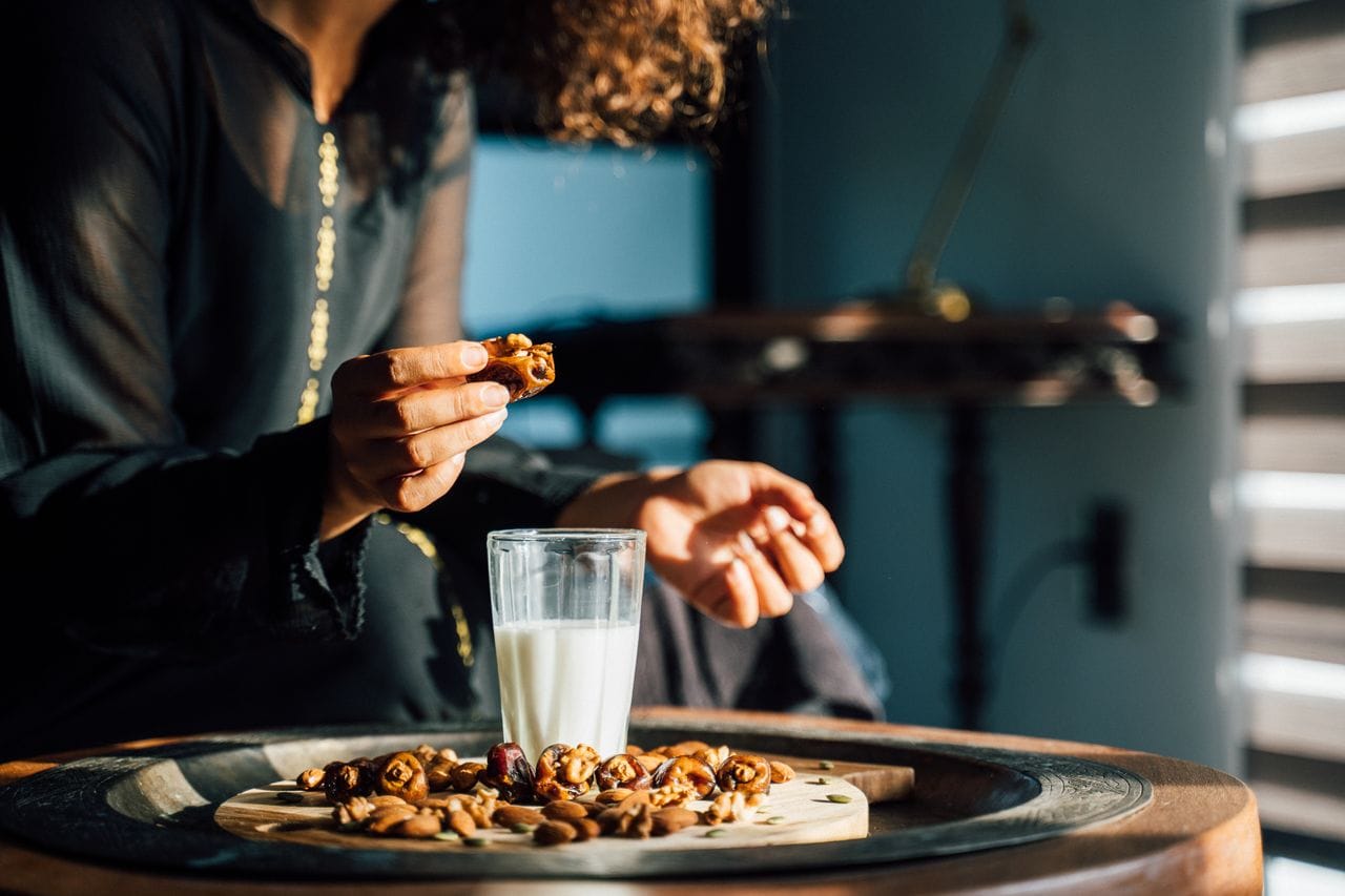 A woman enjoying dates and a glass of milk with sunlight streaming in indoors.