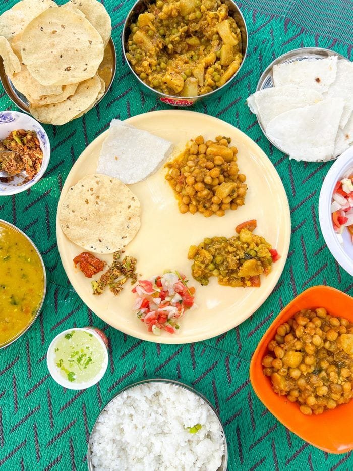 A vibrant Indian thali platter with chickpeas, chutneys, and roti on a colorful tablecloth.