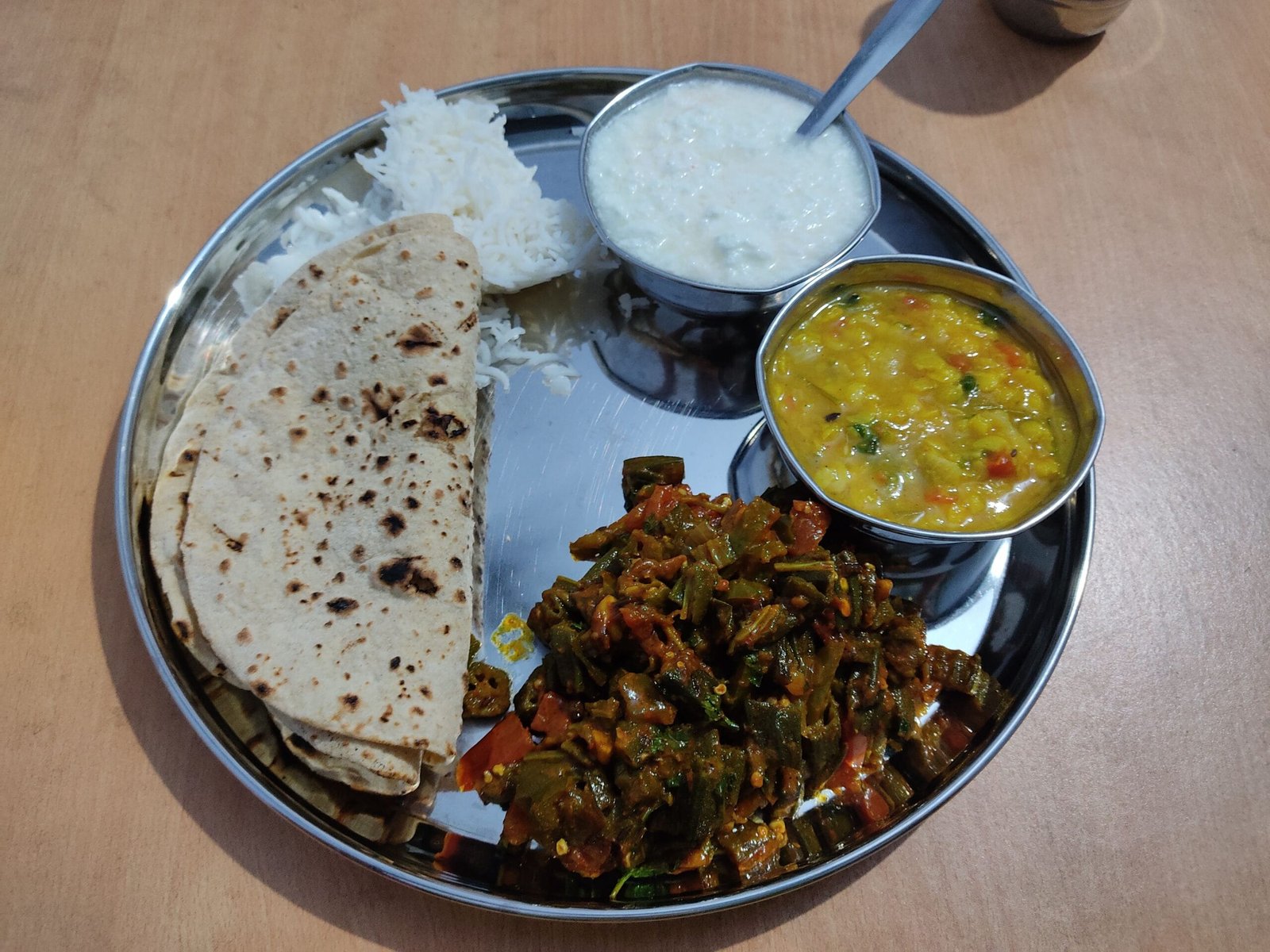 Delicious Indian thali with chapati, rice, dal, okra, and yogurt. A traditional vegetarian meal.